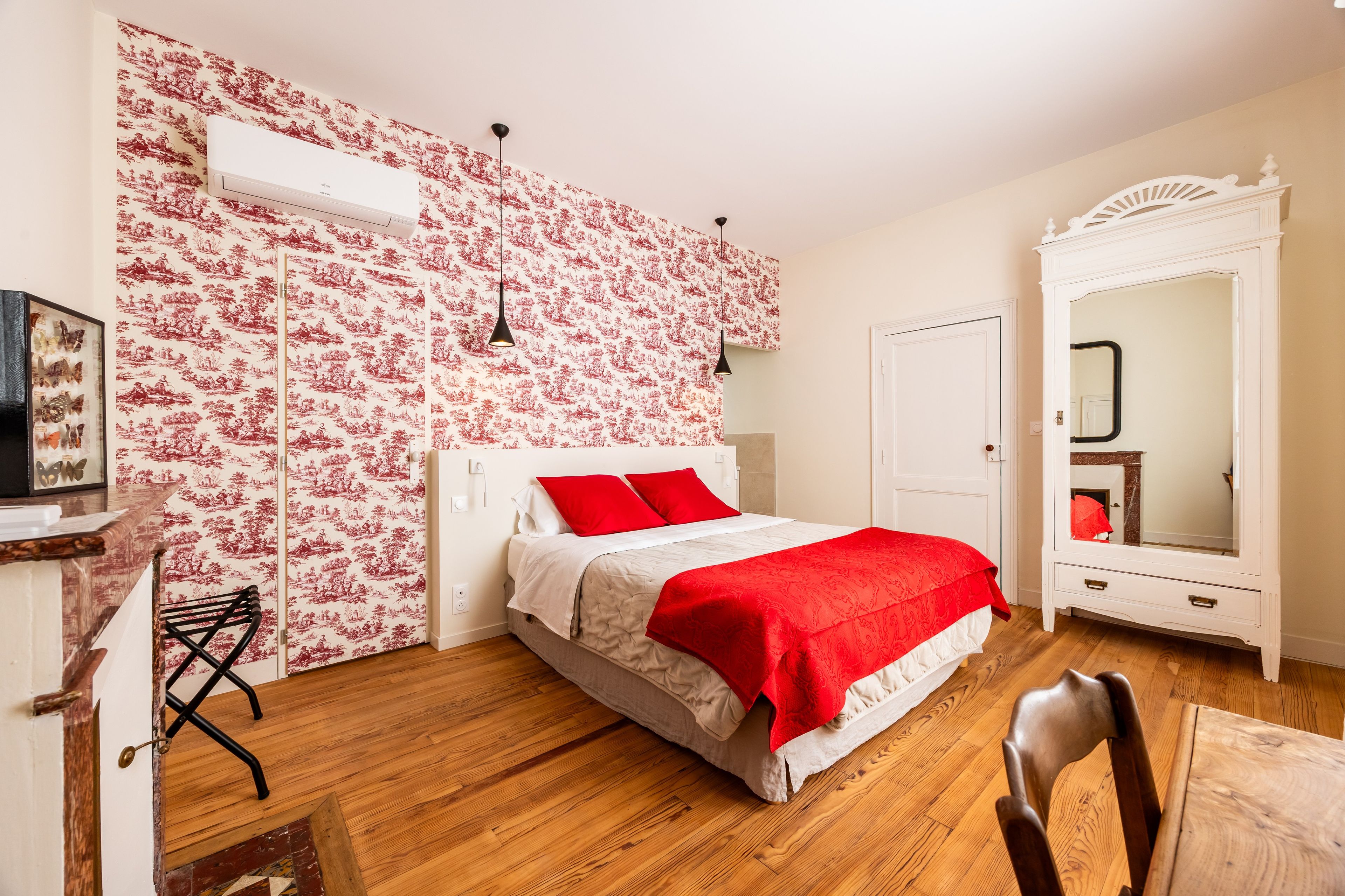 Ein Schlafzimmer mit einem Bett, einem Kleiderschrank, einem Spiegel und einer Wand mit einem Blumenmuster.