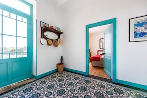 Un pasillo con baldosas de diseño, una puerta azul y un espejo con sombreros en la pared.
