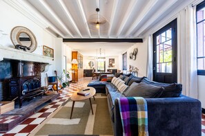 Ein gemütliches Wohnzimmer mit kariertem Boden, Kamin, einer Couch und einem Essbereich im Hintergrund.