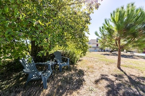 Een terras met twee stoelen en een tafel, omgeven door groen en een gebouw op de achtergrond.