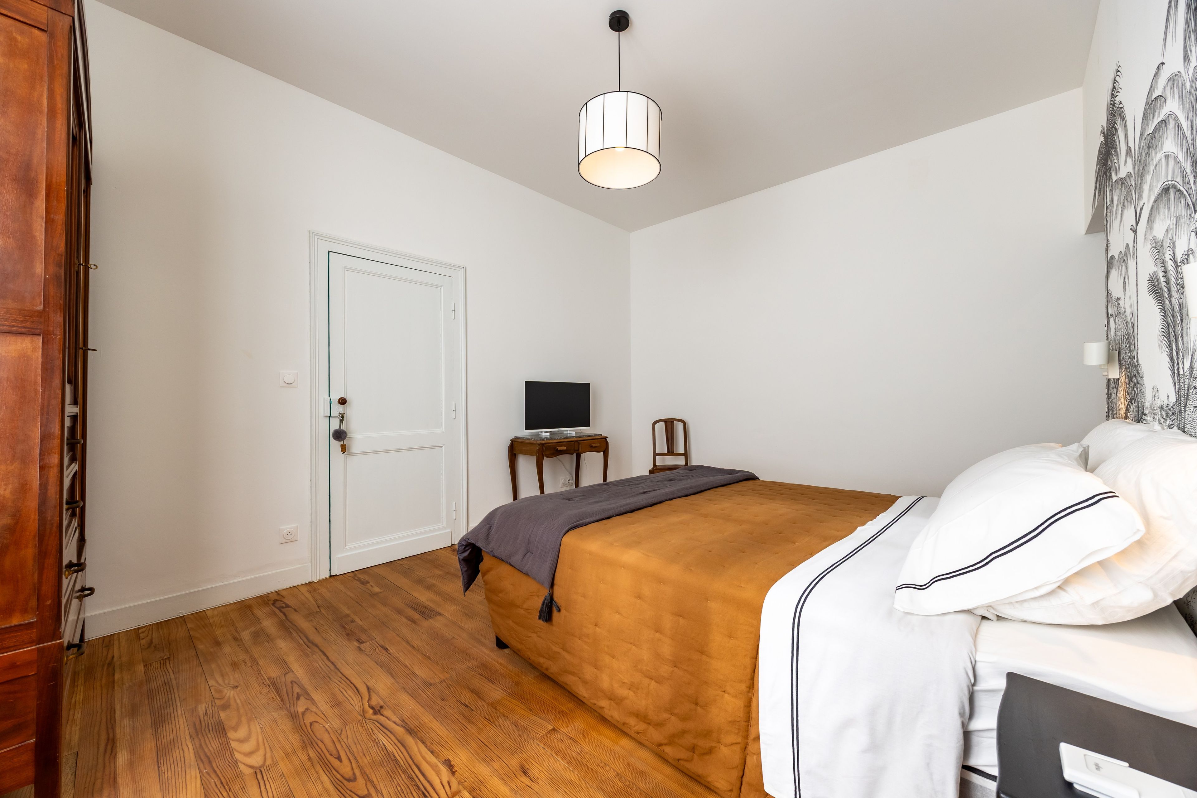 A bedroom with a bed, a desk, a chair, a television, and a wardrobe.