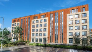 A multi-story building with a mix of brick and wooden facade, large windows, and a parking lot with marked spaces. - Student Only Luneside (Lancaster)