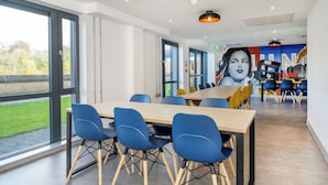 A modern dining area with a large table and blue chairs, large windows, and a mural on the wall. - Student Only Luneside (Lancaster)