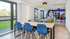 A modern dining area with a large table and blue chairs, large windows, and a mural on the wall. - Student Only Luneside (Lancaster)