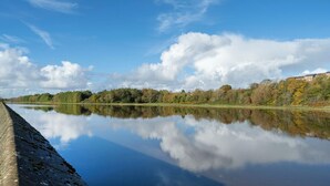 A calm river with a concrete embankment on one side and a forested area on the other. - Student Only Luneside (Lancaster)