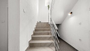 A staircase with a metal railing, white walls, and a small window with a plant. - Stunning home in Kakma (Kakma)