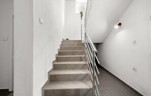 Eine Treppe mit Metallgeländer, weißen Wänden und einem kleinen Fenster mit Pflanze.