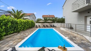 A swimming pool with lounge chairs and umbrellas, surrounded by greenery and buildings. - Stunning home in Kakma (Kakma)