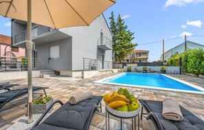 A swimming pool with lounge chairs and a fruit bowl, surrounded by a modern building with a balcony. - Stunning home in Kakma (Kakma)