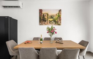 A dining area with a wooden table, six grey chairs, a black refrigerator, a painting of a landscape, a vase with pink flowers, and a bottle of champagne. - Stunning home in Kakma (Kakma)