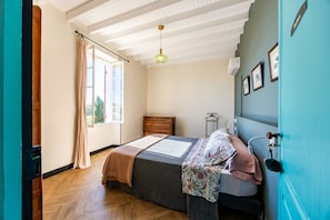 Ein Schlafzimmer mit einem Bett, einer Holzkommode, einer Pendelleuchte und einem Fenster mit Vorhängen.