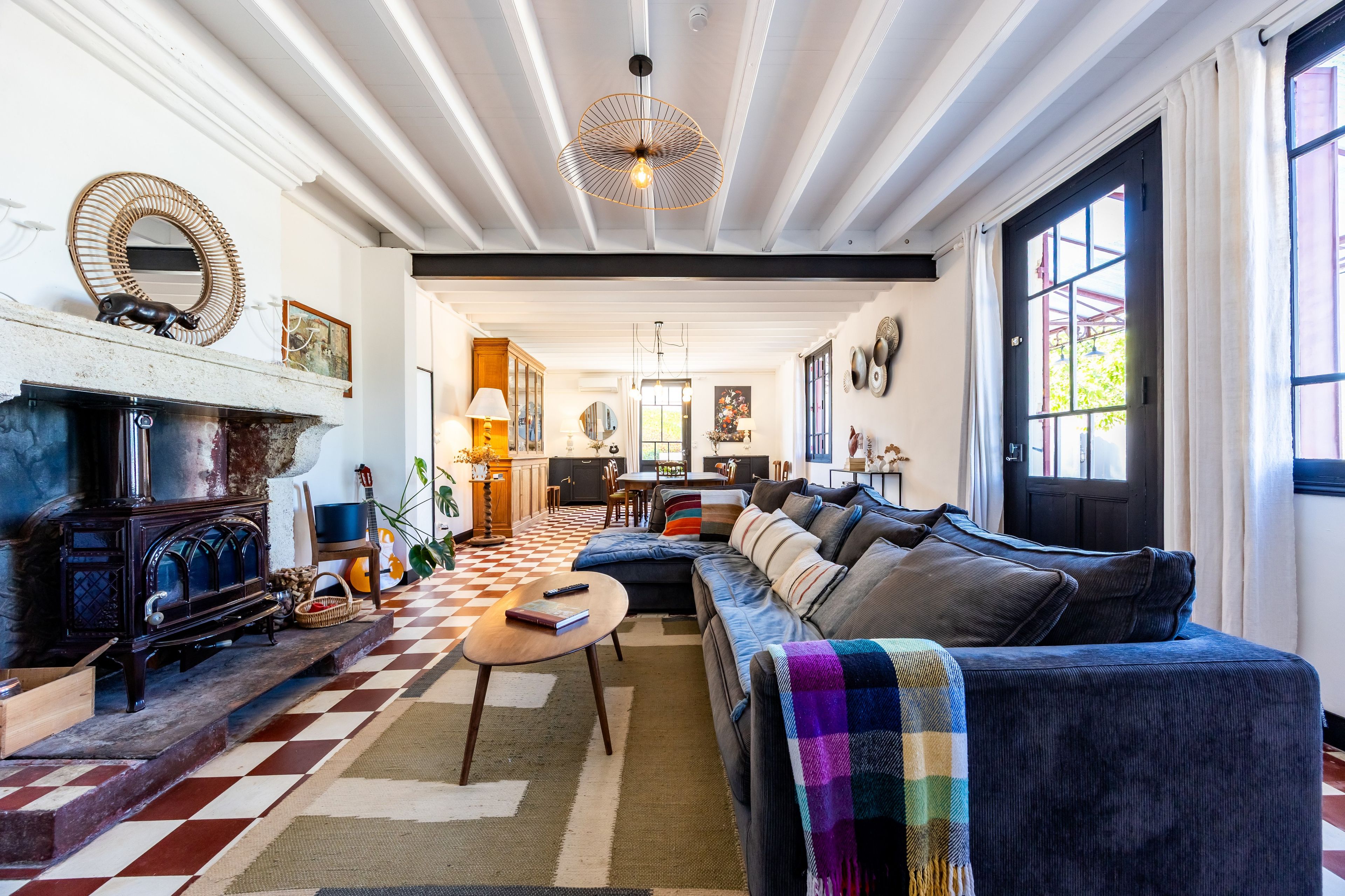 A cozy living room with a checkered floor, a fireplace, a sofa, and a dining area in the background.