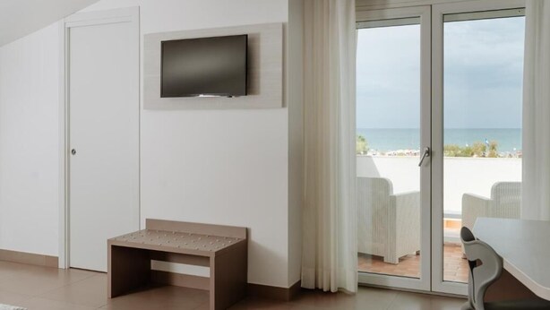 Una habitación moderna con televisión montada en la pared, un banco y vistas a la playa a través de un ventanal corredizo.