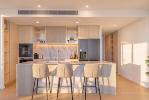 A modern kitchen with a central island, bar stools, built-in appliances, and a sleek design. - Amaya Broadbeach Luxury Stays (Broadbeach)