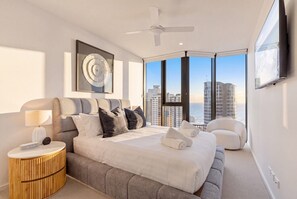 Ein modernes Schlafzimmer mit einem großen Bett, einem runden Nachttisch, einem Sessel und Blick auf die Stadt.