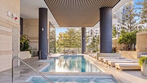 En swimmingpool med ett soldeck, omgiven av modern arkitektur och växter.