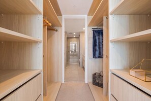 Un couloir étroit, avec des étagères en bois de chaque côté, qui mène à un espace comprenant des toilettes et un lavabo.