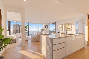 A modern kitchen with a marble island, large windows, and a view of the city. - Amaya Broadbeach Luxury Stays (Broadbeach)