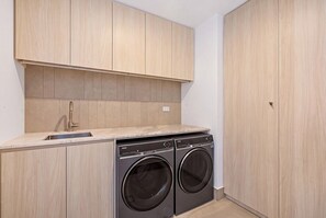 Une petite buanderie comprenant un lave-linge et un sèche-linge, des armoires en bois et un plan de travail avec un évier.