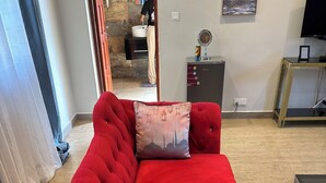 Ein rotes Sofa mit einem dekorativen Kissen, ein kleiner Tisch mit einer Lampe und ein Fernseher auf einem Schrank.
