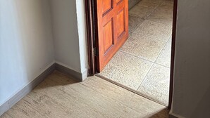 Eine Holztür führt in einen Raum mit Fliesenboden und einer Steinwand.