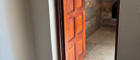 Una puerta de madera que da a un espacio con suelo de baldosas y pared de piedra.