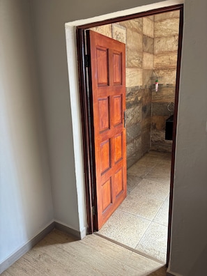 Una puerta de madera que da a un espacio con suelo de baldosas y pared de piedra.
