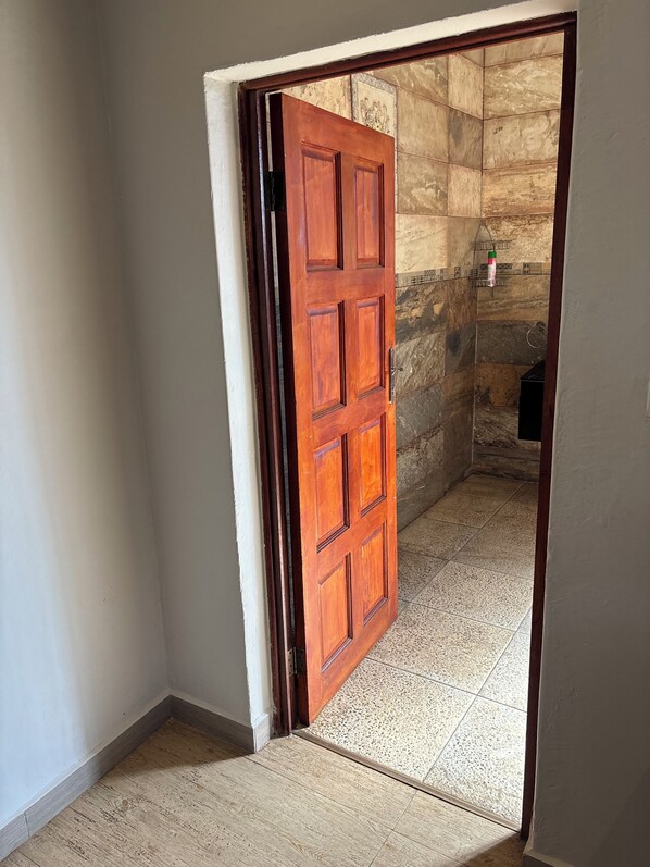 Una puerta de madera que da a un espacio con suelo de baldosas y pared de piedra.