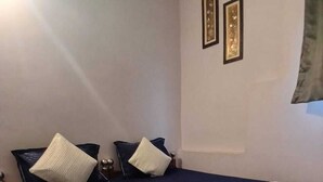 Quarto de hotel com cama, almofadas, colcha azul e duas fotos emolduradas na parede.