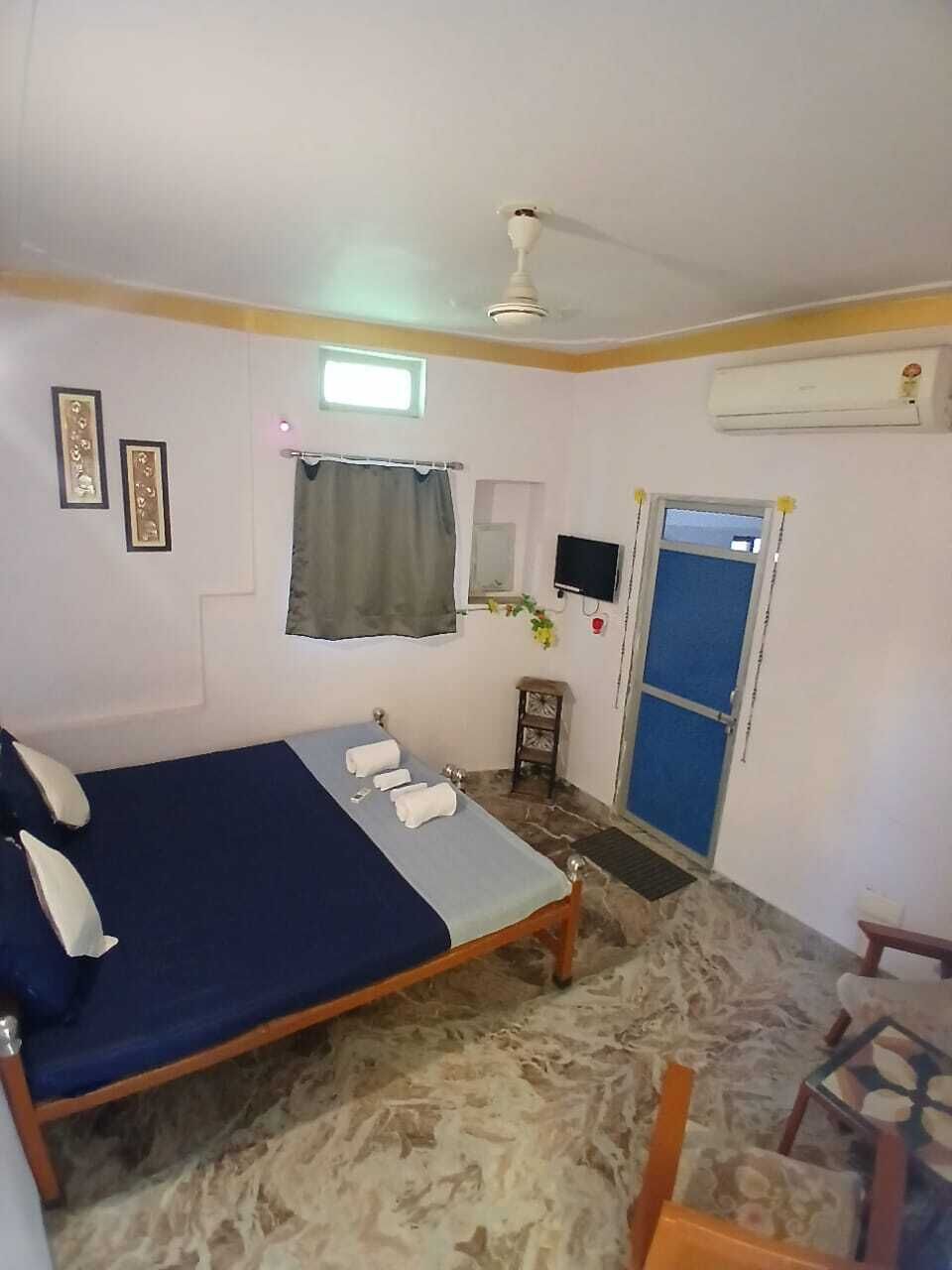 A bedroom with a bed, a ceiling fan, a window, a door, and a small table with a chair.