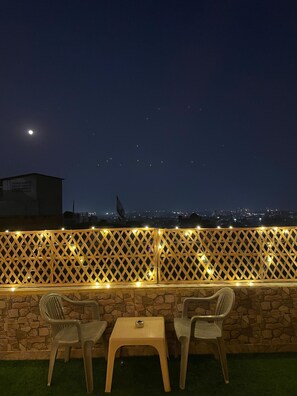 An outdoor seating area with two chairs and a table, a stone wall, and a view of a cityscape at night. - Stayostel (Udaipur)