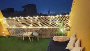 Um terraço no telhado com uma cama, uma mesa, cadeiras e um muro de pedra.