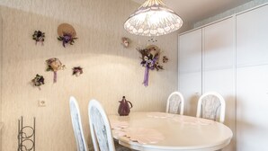 Comedor con una mesa redonda, sillas blancas, una araña y adornos florales en la pared.