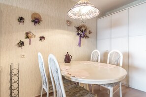 Comedor con una mesa redonda, sillas blancas, una araña y adornos florales en la pared.