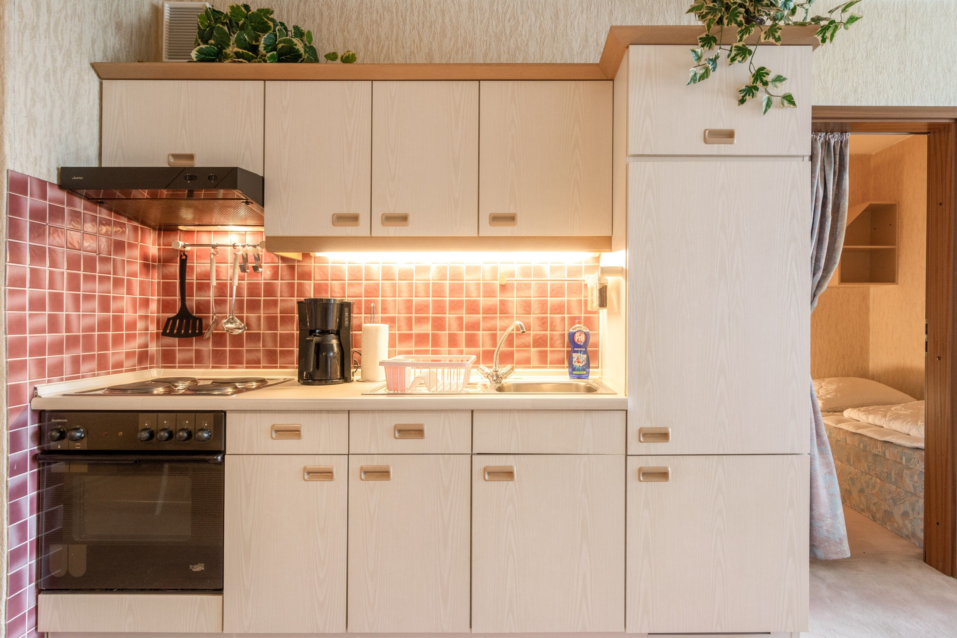 Eine kompakte Küche mit Herd, Backofen und Spüle, Holzschränken und einer gefliesten Rückwand.