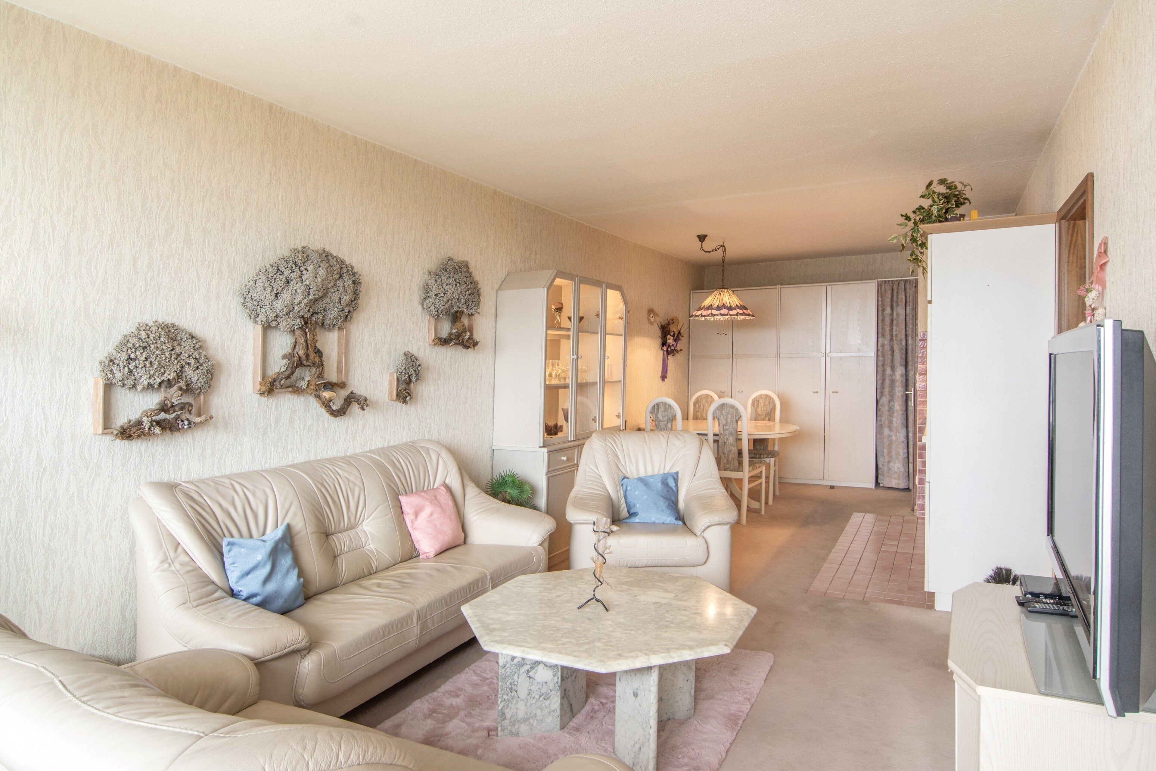 A living room with a beige sofa, a coffee table, and a dining area with chairs and a table.
