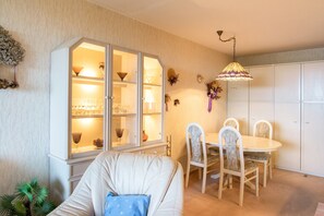 Un comedor con una mesa redonda y sillas, un aparador con puertas de vidrio, y una lámpara colgante.