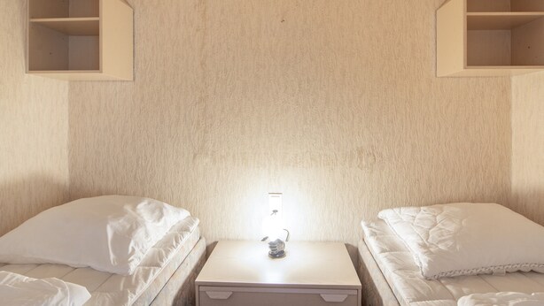 Una habitación con dos camas, una mesita de noche con lámpara y estanterías empotradas sobre las camas.