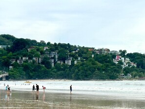 Una zona costera con edificios en una colina y gente en la playa.