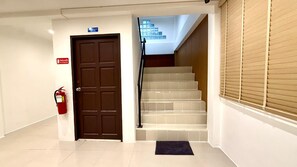 Um corredor de hotel com um extintor de incêndio, uma porta com a inscrição 'Apenas para funcionários' e uma escadaria.