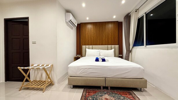 A hotel room with a bed, a wooden headboard, a window with curtains, a wall-mounted air conditioner, and a small wooden drying rack. - King Bed Beachfront Retreat Patong (Tambon Patong)