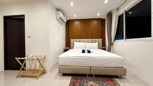 Ein Hotelzimmer mit Bett, Holz-Kopfseitenverkleidung, einem Fenster mit Vorhängen, einer wandmontierten Klimaanlage und einem kleinen Wäscheständer.
