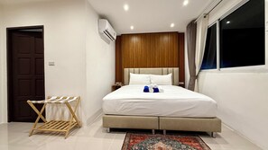 A hotel room with a bed, a wooden headboard, a window with curtains, a wall-mounted air conditioner, and a small wooden drying rack. - King Bed Escape by Patong Beach (Tambon Patong)