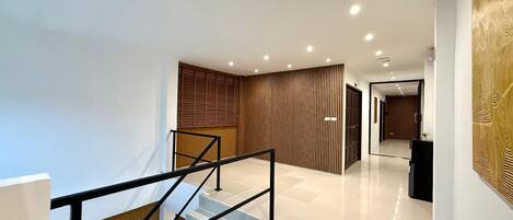 A modern interior with a staircase, a wooden panel wall, and a hallway leading to another room.