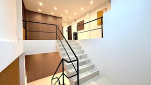 Een trap met een modern ontwerp, voorzien van een zwarte metalen balustrade en houten lambrisering aan de wanden.