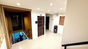 A hotel corridor with a staircase leading to a lower level, a door with a sign, a water dispenser, and a patterned wall. - Patong Beachfront Relaxing Stay (Tambon Patong)