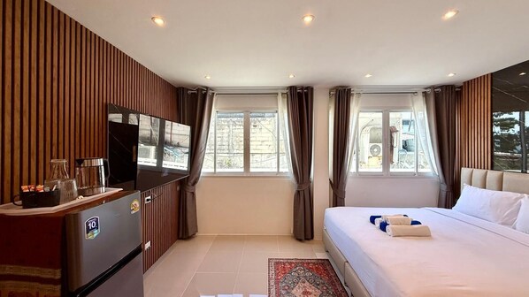 A hotel room with a bed, a TV, a minibar, and a window with curtains. - Patong Beachfront Relaxing Stay (Tambon Patong)