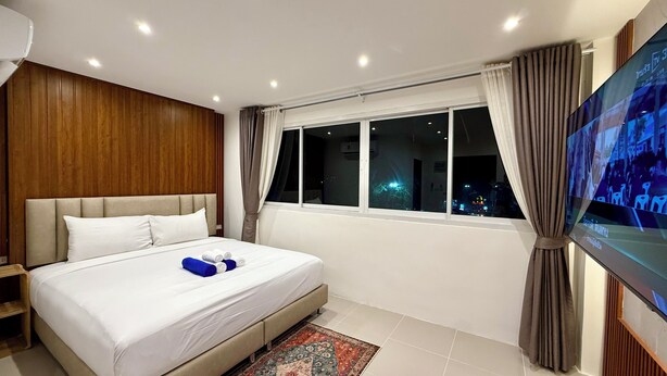 Een hotelkamer met een bed, een televisie, een raam met gordijnen en een houten wand.