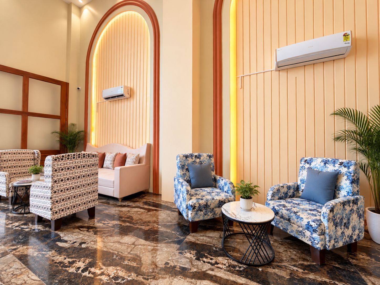 A hotel lobby with a seating area featuring patterned sofas and armchairs, a marble floor, and an air conditioning unit mounted on the wall.