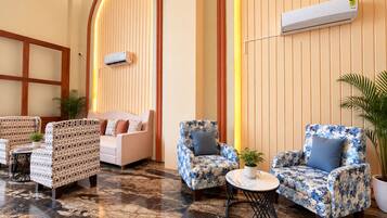 A hotel lobby with a seating area featuring patterned sofas and armchairs, a marble floor, and an air conditioning unit mounted on the wall.